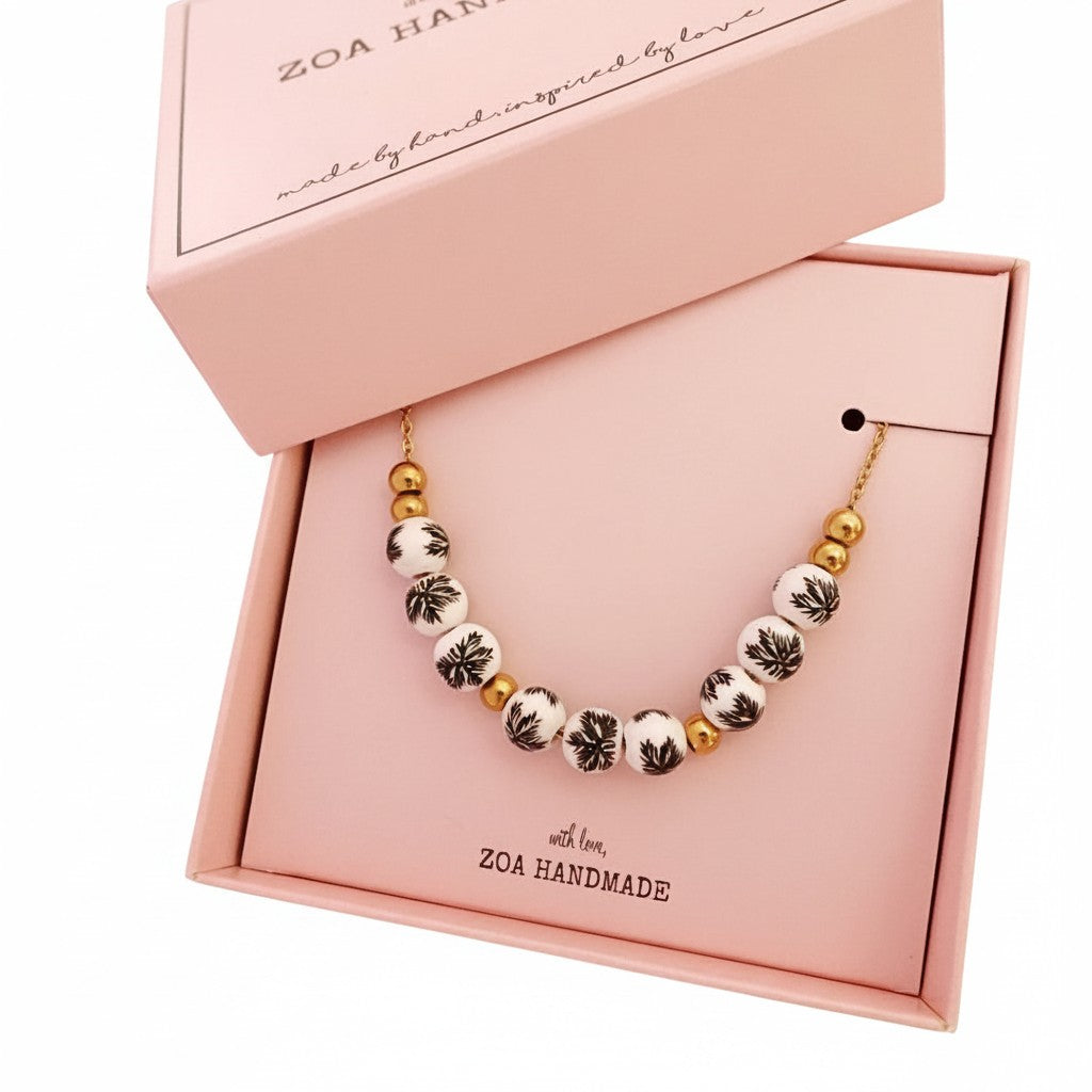 ZOA HANDMADE gold chain necklace with hand-painted white ceramic beads featuring black floral designs and gold accents.